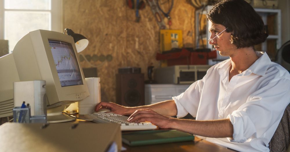 Male Stock Trader Using Old Desktop Computer With Financial Candlestick Chart In Retro Garage.