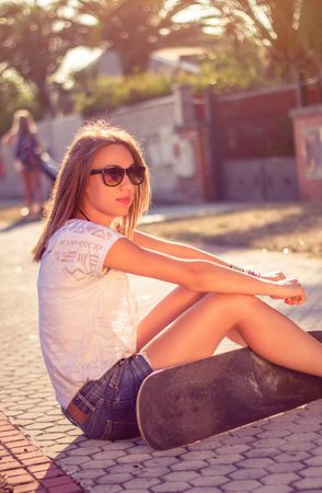 Young girl with skateboard sitting outdoors on summer