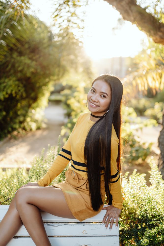 Long haired Asian woman sitting on back of bench in park