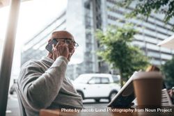 Man in eyeglasses sitting in a street side restaurant talking on mobile phone and reading a book 5lnrMb