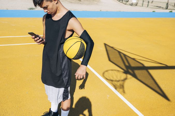Male basketball player using his smartphone resting after training