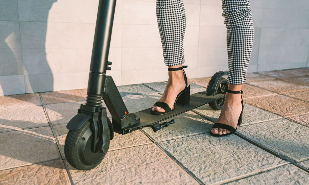 Unrecognizable businesswoman legs with e-scooter outdoors