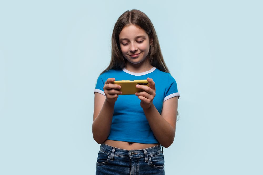 Girl holding smartphone, engaged and focused, possibly gaming or browsing.