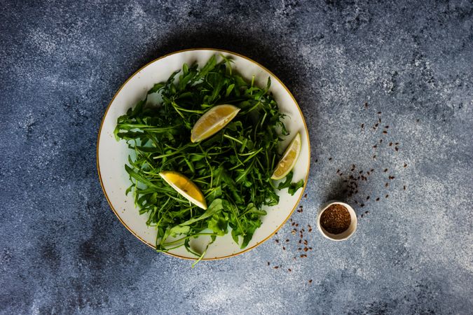 Top view of healthy vegetable salad with organic arugula, lemon and flax seeds on stone background with copy space