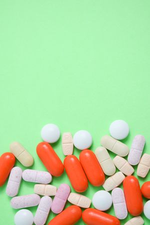 Top view of variety of colorful medication and vitamins on green table with copy space