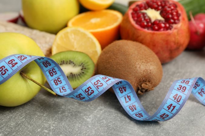 Measuring tape and vegetarian food on gray background, close up