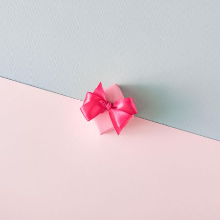 Gift box with pink ribbon on baby blue and baby pink background
