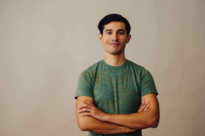 Hispanic male standing in neutral room with arms crossed