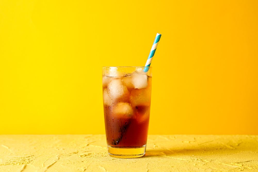 Glass with cold cola and tubule against yellow background