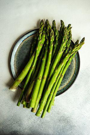 Loose raw asparagus on plate on marble counter