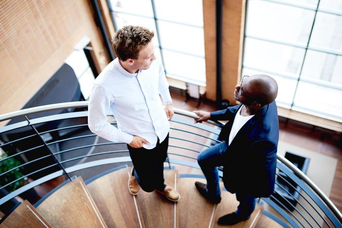 Two businessmen stopped to talk on a staircase in an office