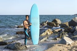 Male surfer standing in the rocks on the coast