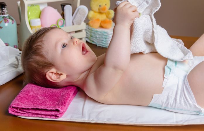 Side view of cute baby playing with towel during diaper change