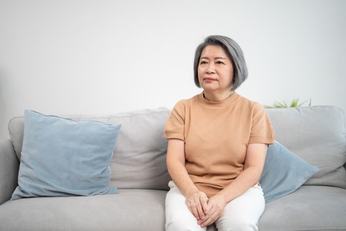 Single older Asian female sitting on couch at home