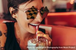 Close up of a smiling  woman in star shaped fancy eyeglasses drinking a milkshake 0LOZgb
