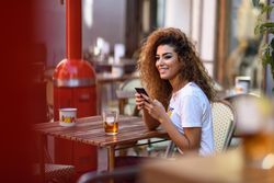 Arab woman in casual clothes using her phone on cafe patio