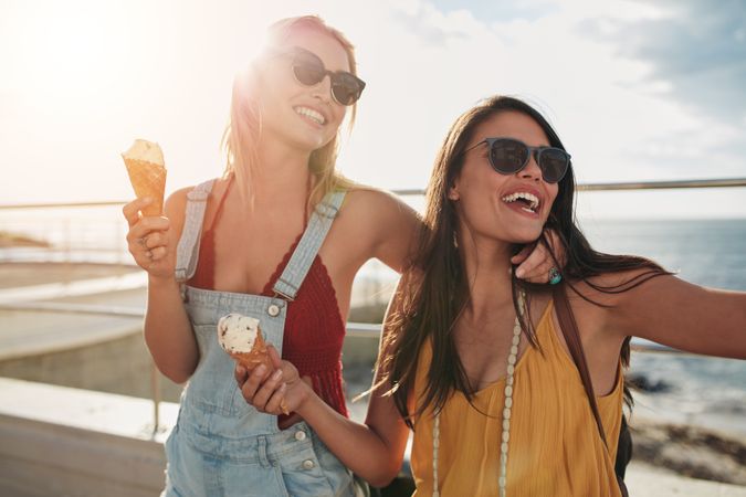 Close up of cheerful young women eating ice cream at seaside promenade
