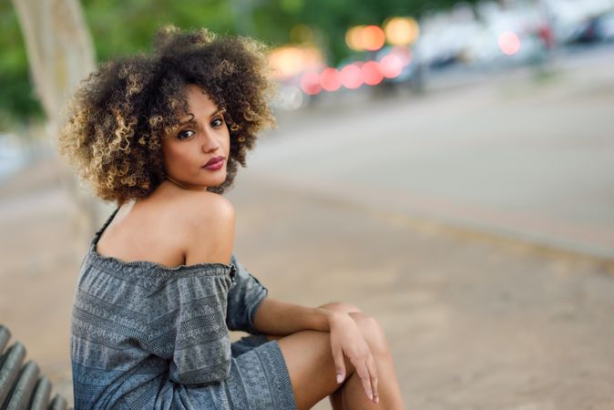 Serious female in casual dress sitting on park bench looking around, copy space