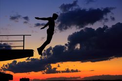 Silhouette side view of male at dusk jumping off roof