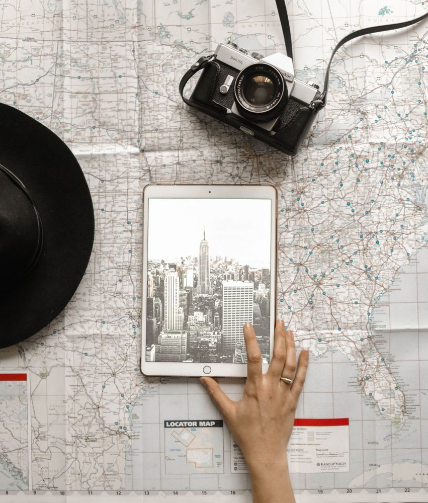 Top view of hand touch a tablet computer with NY cityscape on a map near hat and camera