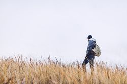 Man walking between sand field with dry grass