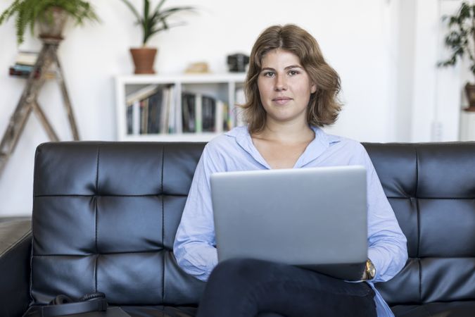 Calm woman sitting on a sofa at home working on a laptop