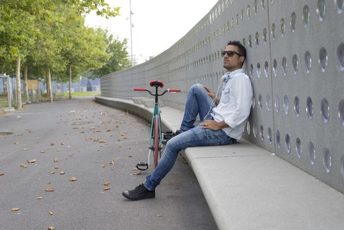 Male in sunglasses sitting outside of park with bicycle