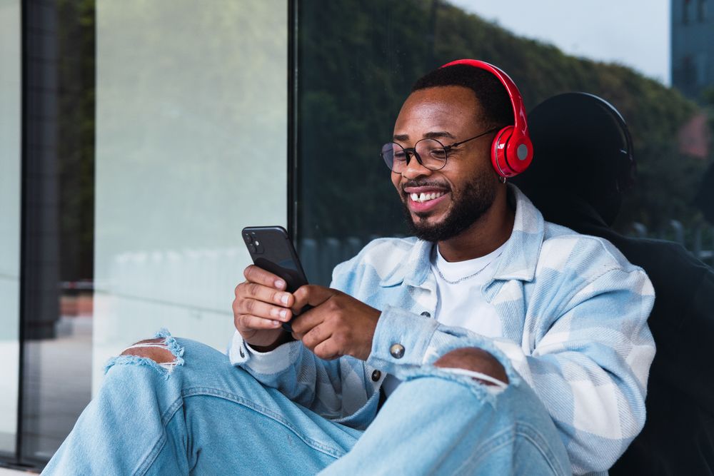 Cheerful Black man with smartphone listening to music