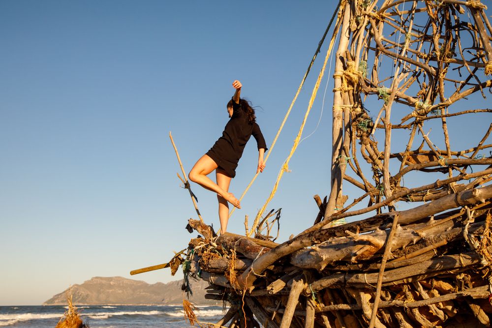 Young woman with upped leg on decorative wooden ship near water on shore