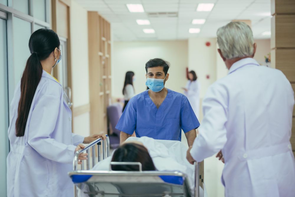 Group of medical staff wheeling patient in bed through hospital