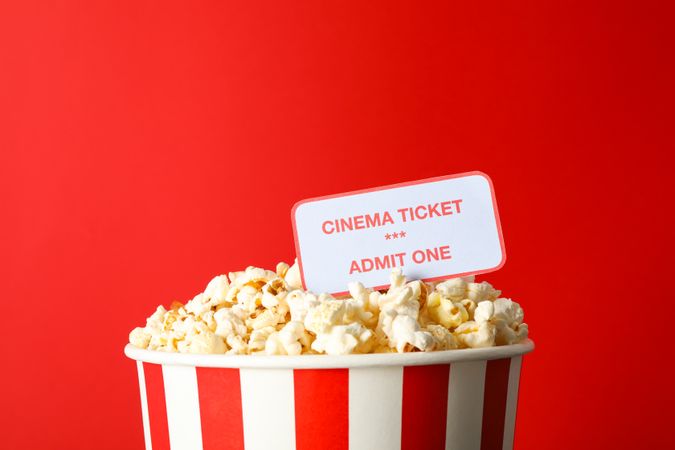 Striped bucket with popcorn and tickets against red background