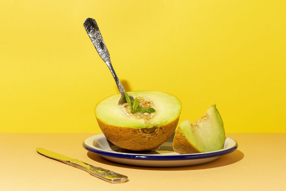 Sliced small melon on plate with spoon and fork