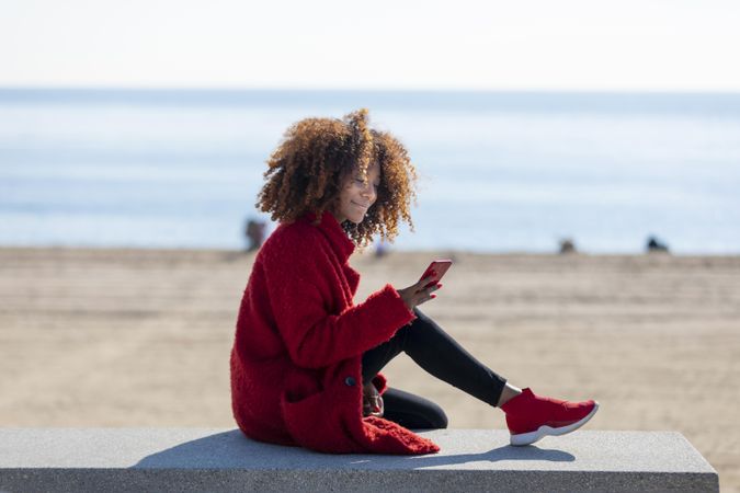 Side view of female checking smart phone on bench on a beach
