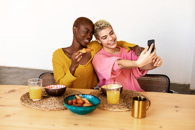 Two female friends taking selfie at breakfast together at home