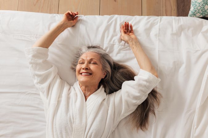 Grey haired woman relaxing on bed smiling with eyes closed