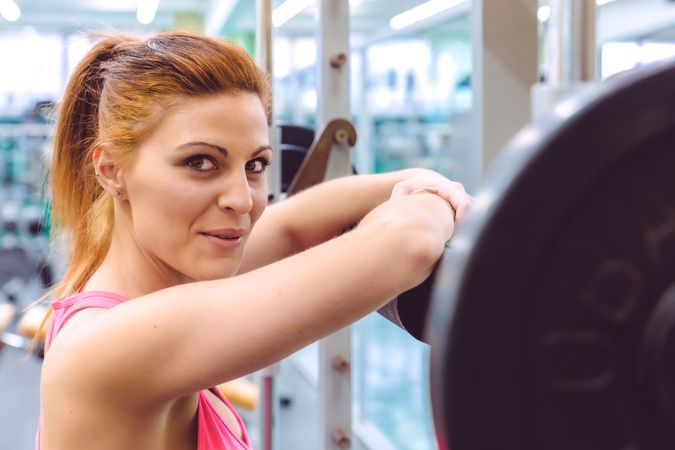 Proud red haired woman leaning on barbell in gym