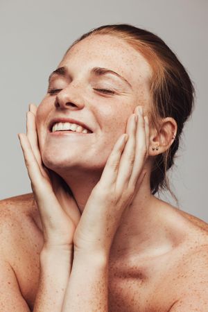 Close up of smiling woman with hands on face and closed eyes