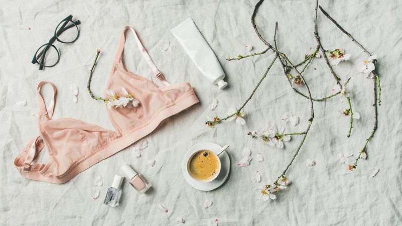 Woman’s bralette top, eyeglasses, cream, and nail polish over textured background