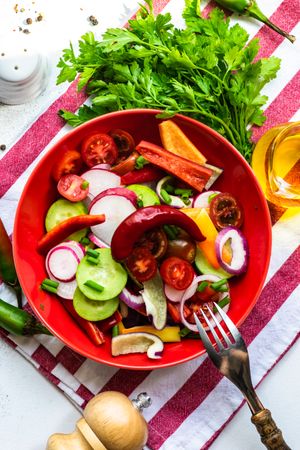 Top view of colorful healthy raw vegetable salad served in red bowl on striped napkin