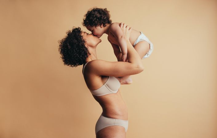 Woman with curly hair holding up her baby and kissing her