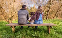 Back of parents with small girl on park bench looking out to forest