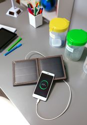Mobile phone charging with portable solar panel and selective trash bins over desk in classroom