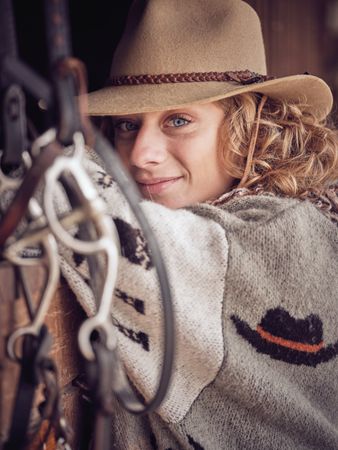 Smiling horsewoman in hat standing in stall