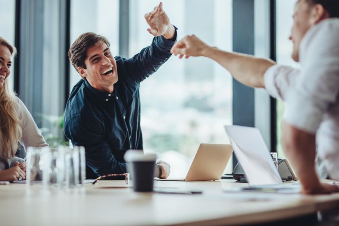 Excited professional reaching across table to high five employee