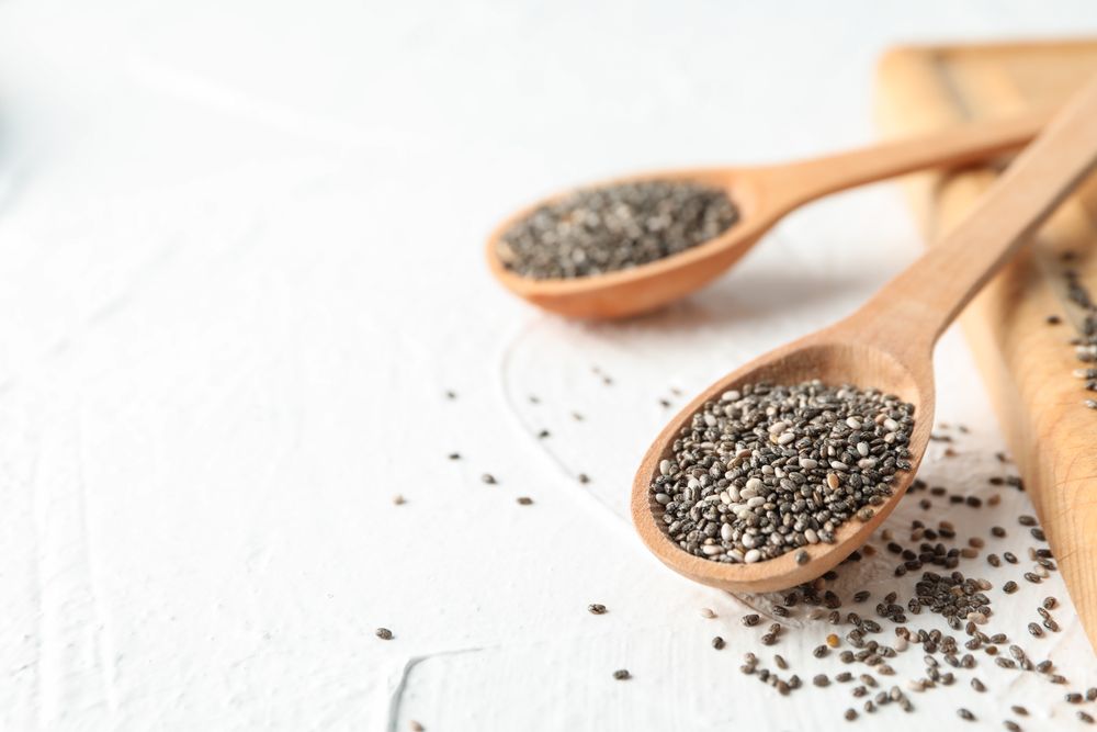 Wooden spoons with chia and board on plain background, close up