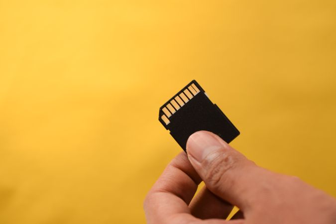 Hand holding SD card for data in yellow studio shoot with copy space