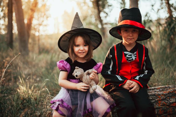 Brother and sister sitting in forest in Halloween costumes