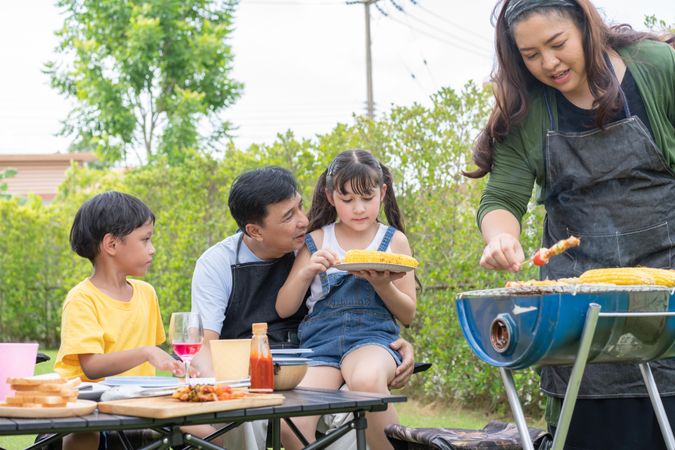 Father talking and playing with kids while mother cooks on the grill