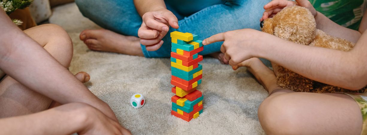 Banner of unrecognizable family having fun playing with stacking piece game over carpet at home