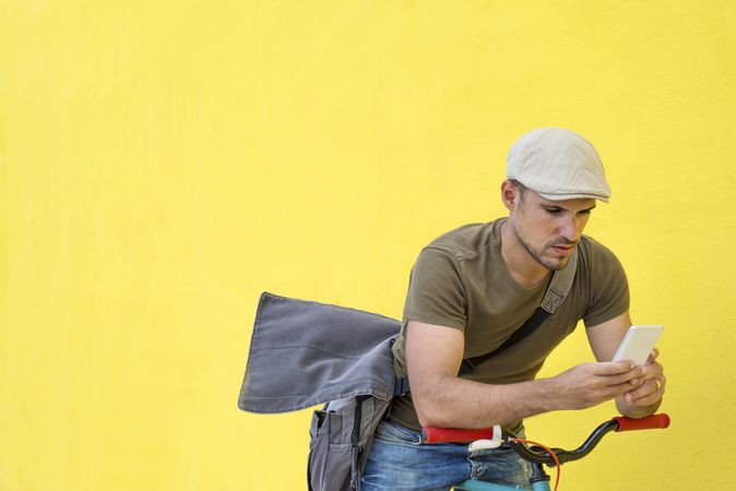 Male in hat and sunglasses using phone while sitting on bicycle